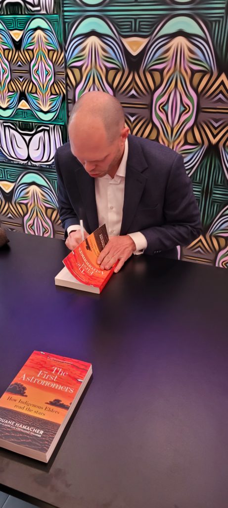 Duane Hamacher at a table signing copies of The First Astronomers